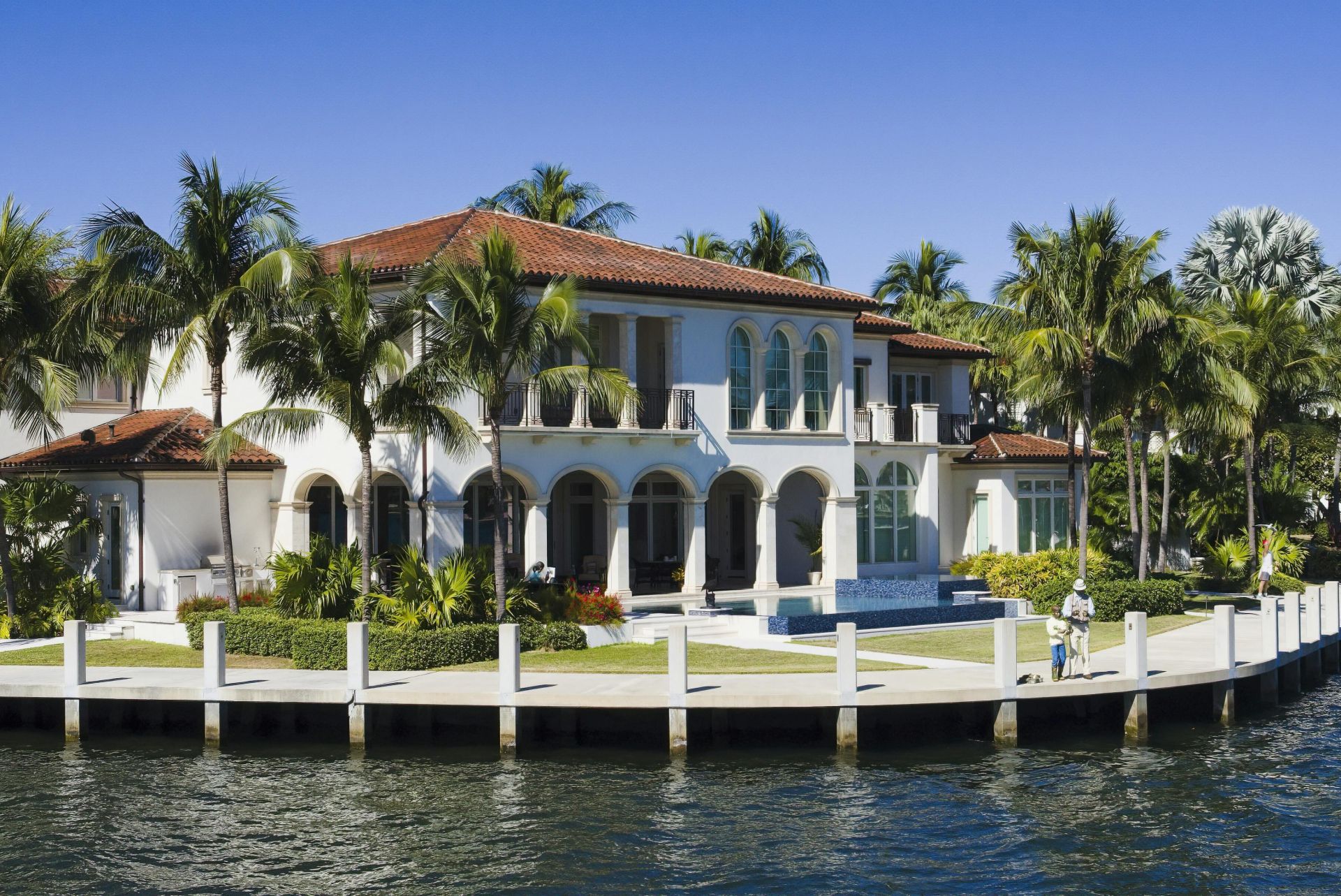 Elegant waterfront mansion in Fort Lauderdale, surrounded by palm trees and bright skies.