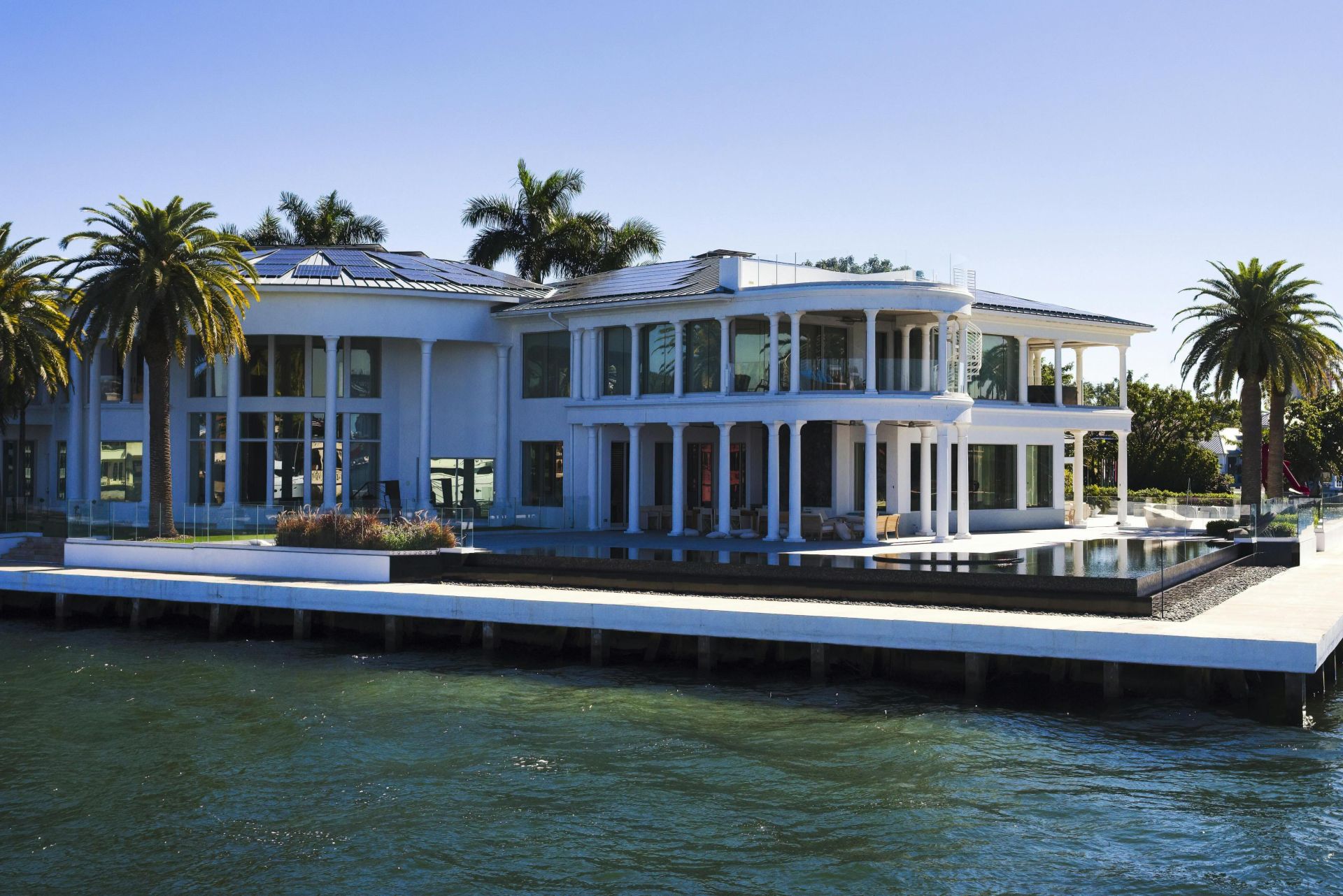 Stunning modern mansion with palm trees by Florida waterfront, perfect for luxury living.